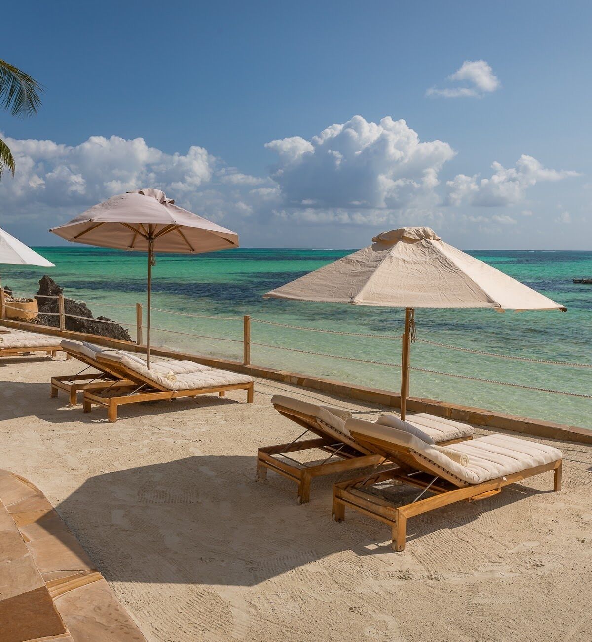 A beach with wooden lounge chairs and white umbrellas.
