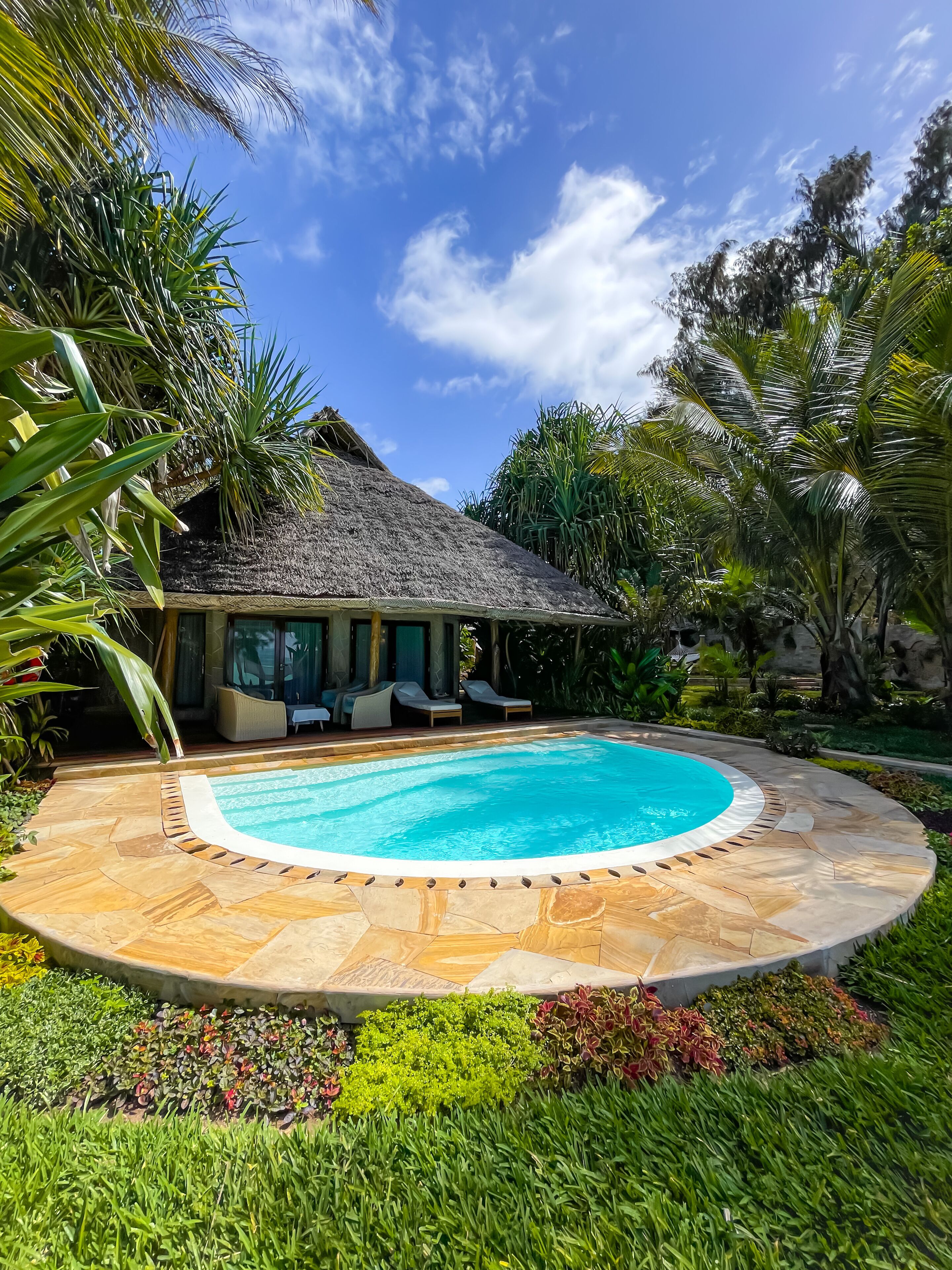 Uma área de piscina com estrutura de telhado de palha, cadeiras de descanso e um jardim bem cuidado.