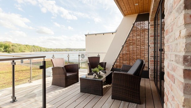 A deck with wicker furniture, a view of the lake, and a brick wall. - Ringelnatz Inselhotel Malchow (Malchow)