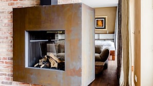 A modern living room with a fireplace, brick wall, and a bed in the background. - Ringelnatz Inselhotel Malchow (Malchow)