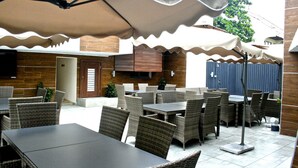 An outdoor dining area with wicker furniture and a large umbrella providing shade. - Scarlet Lodge (Lagos)