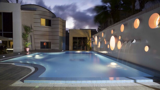 A swimming pool with a modern design, surrounded by a building with circular windows and a curved facade. - Scarlet Lodge (Lagos)