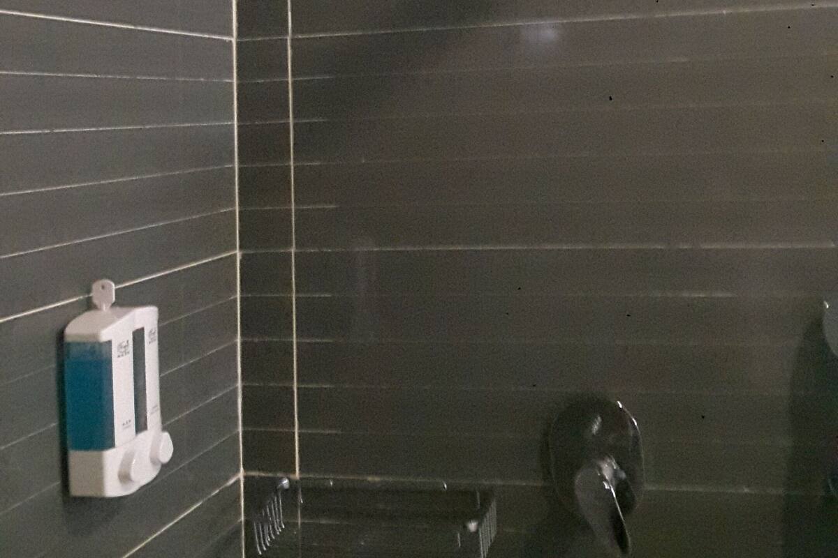 Un bagno con pareti piastrellate scure, un soffione doccia, un dispenser di sapone e un portasciugamani.
