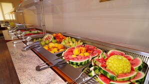 Un bufé con diversas frutas y verduras, incluyendo sandía y piña, dispuesto en un mostrador con utensilios para servir.