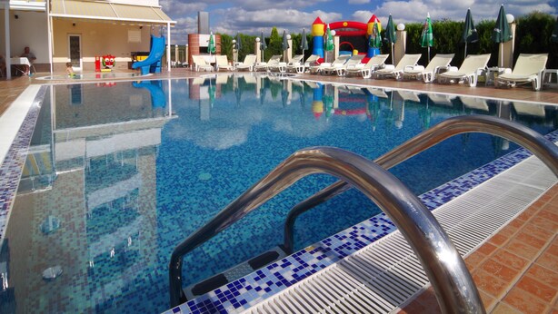 Piscina con tobogán y estructuras inflables para jugar, rodeada de tumbonas y sombrillas.