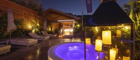 Un jacuzzi rodeado de sillones de descanso y velas, con una valla de madera y una bandera al fondo.