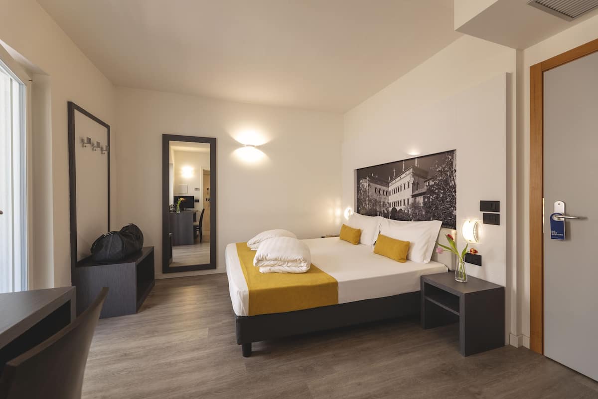 A modern hotel room with a large bed, bedside tables, a desk, and a mirror.