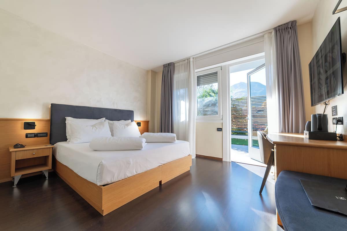 A modern hotel room with a large bed, a desk, and a view of the outdoors.