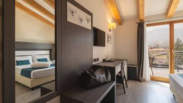 A hotel room with a bed, a desk, a bench, a TV, and a view of the city.