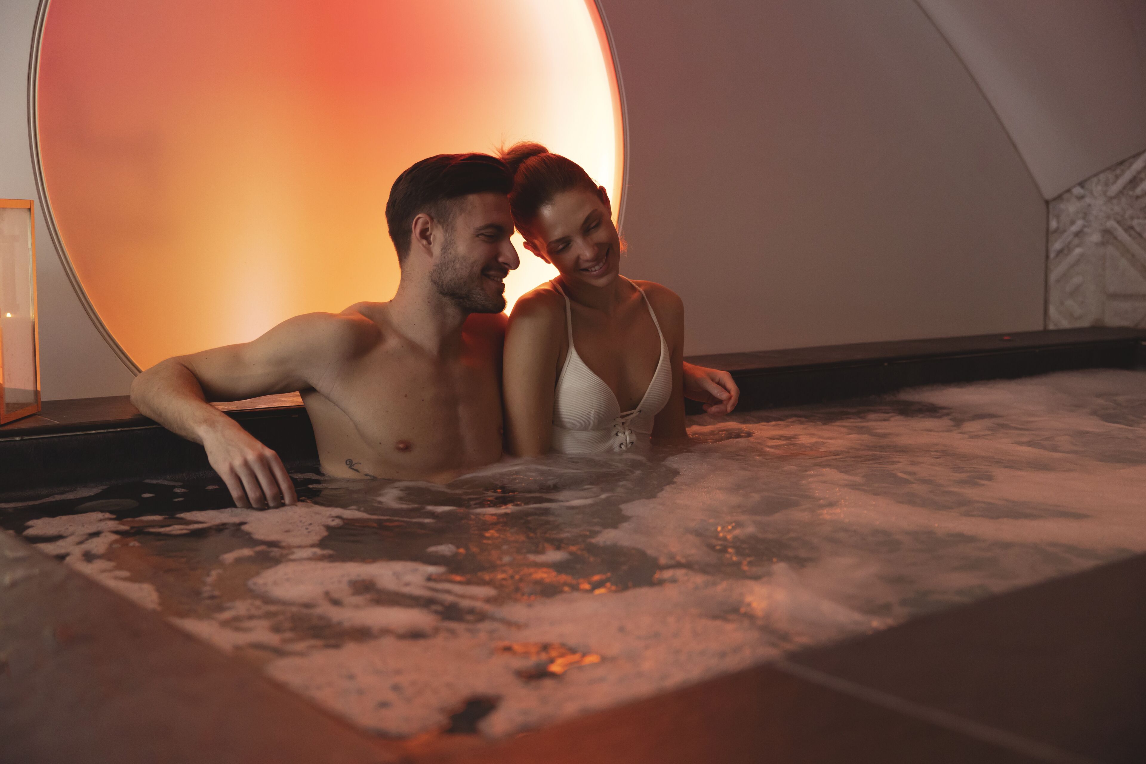 A couple in a hot tub with a circular, illuminated backdrop.