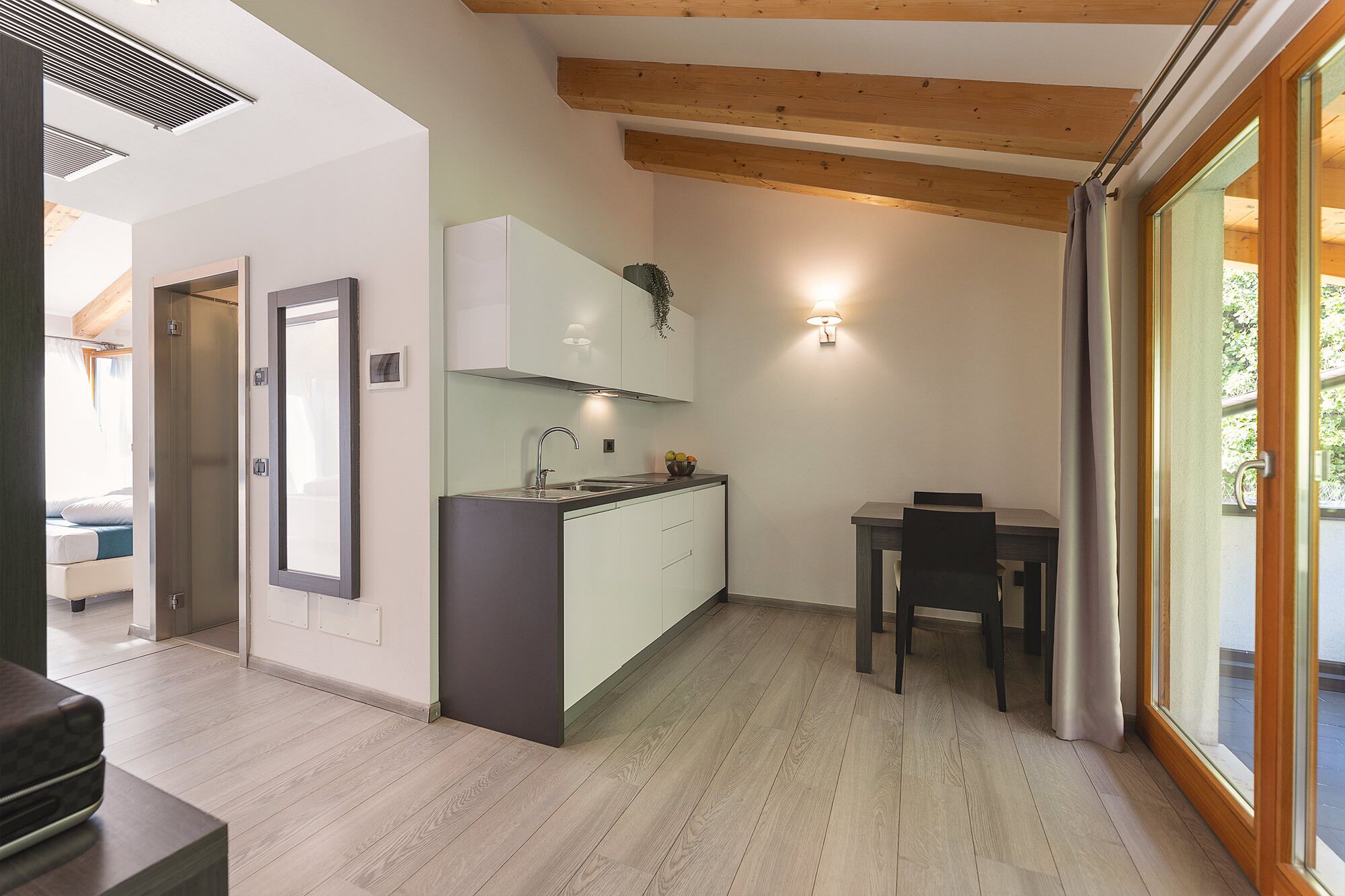 A compact kitchen with a dining area, wooden beams, and a large window.