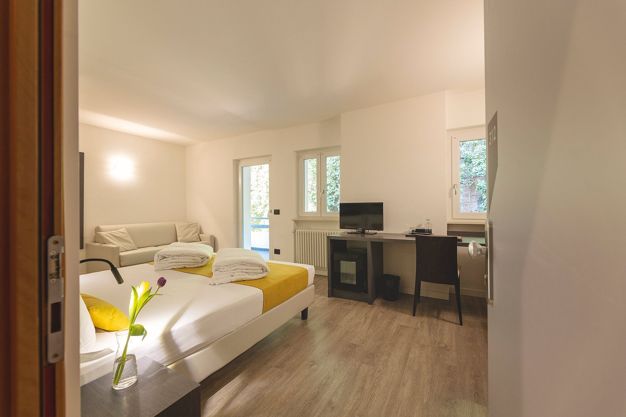 Una habitación de hotel con cama, escritorio, televisor y ventana.