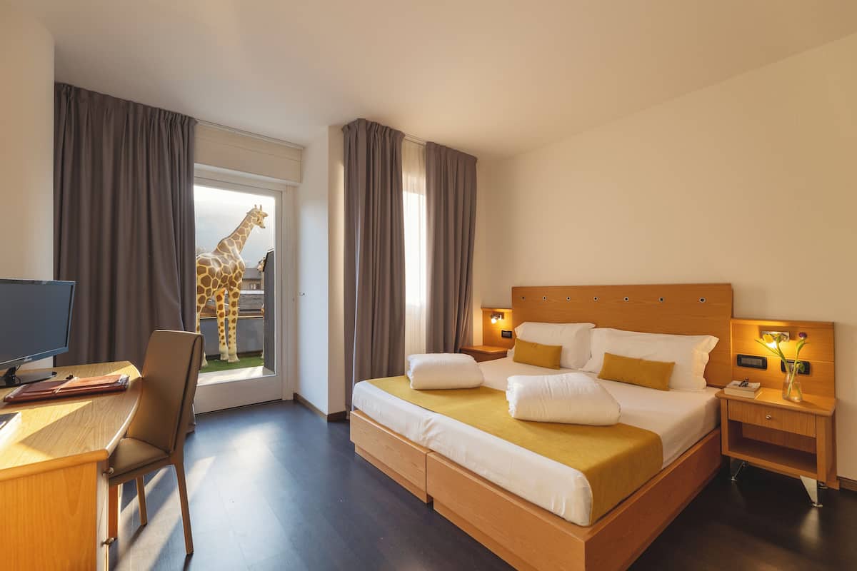A hotel room with a bed, a desk, a chair, a nightstand, and a giraffe statue in the doorway.