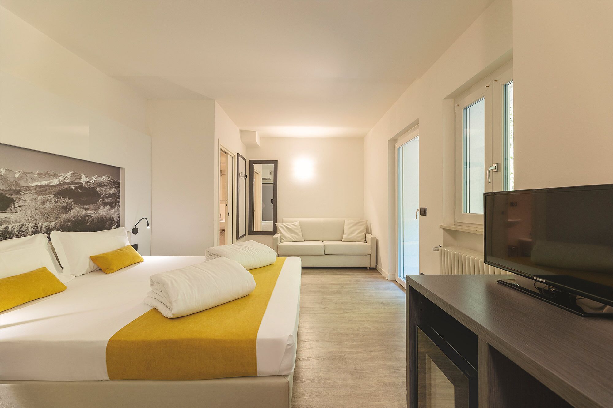 A hotel room with a bed, a sofa, a television, and a large window.