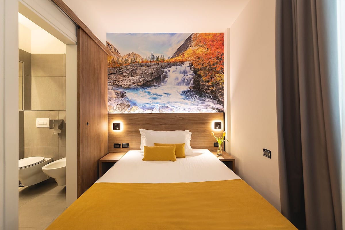 A hotel room with a bed, a bathroom, and a mural of a waterfall.