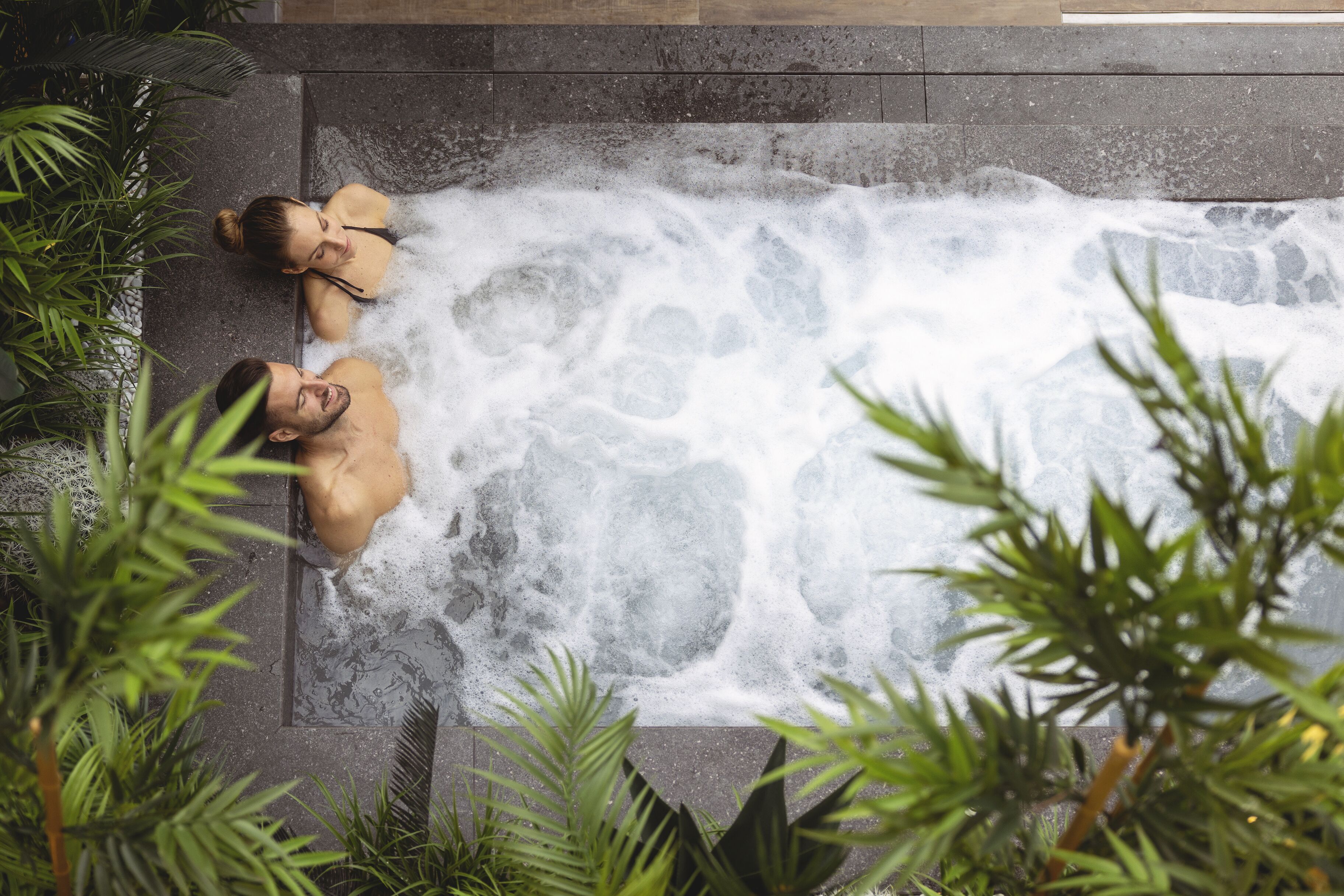 A hot tub with two people, surrounded by greenery.
