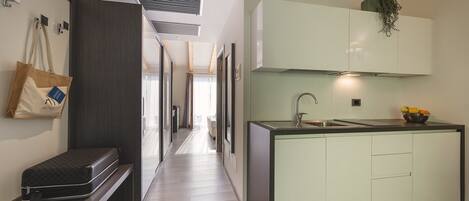 A modern hotel corridor with a built-in bench, a small kitchenette with a sink, and a bag hanging on the wall.
