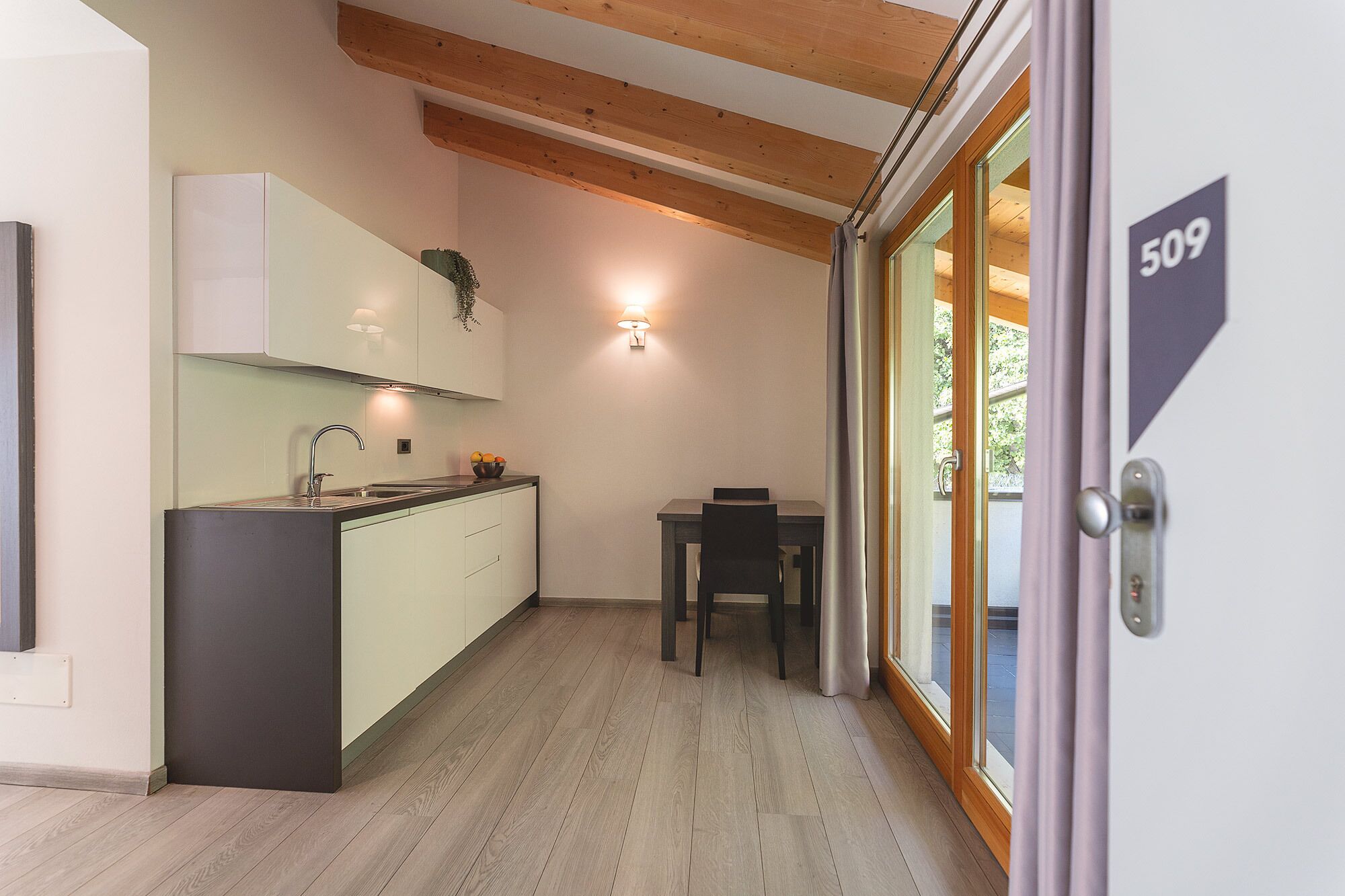 Une cuisine moderne avec un plafond en bois, un coin repas comprenant une table et des chaises, et une porte-fenêtre coulissante donnant sur un espace extérieur.