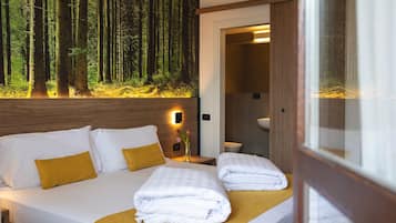 A hotel room with a bed, a nightstand, a vase with flowers, and a wall mural of a forest.