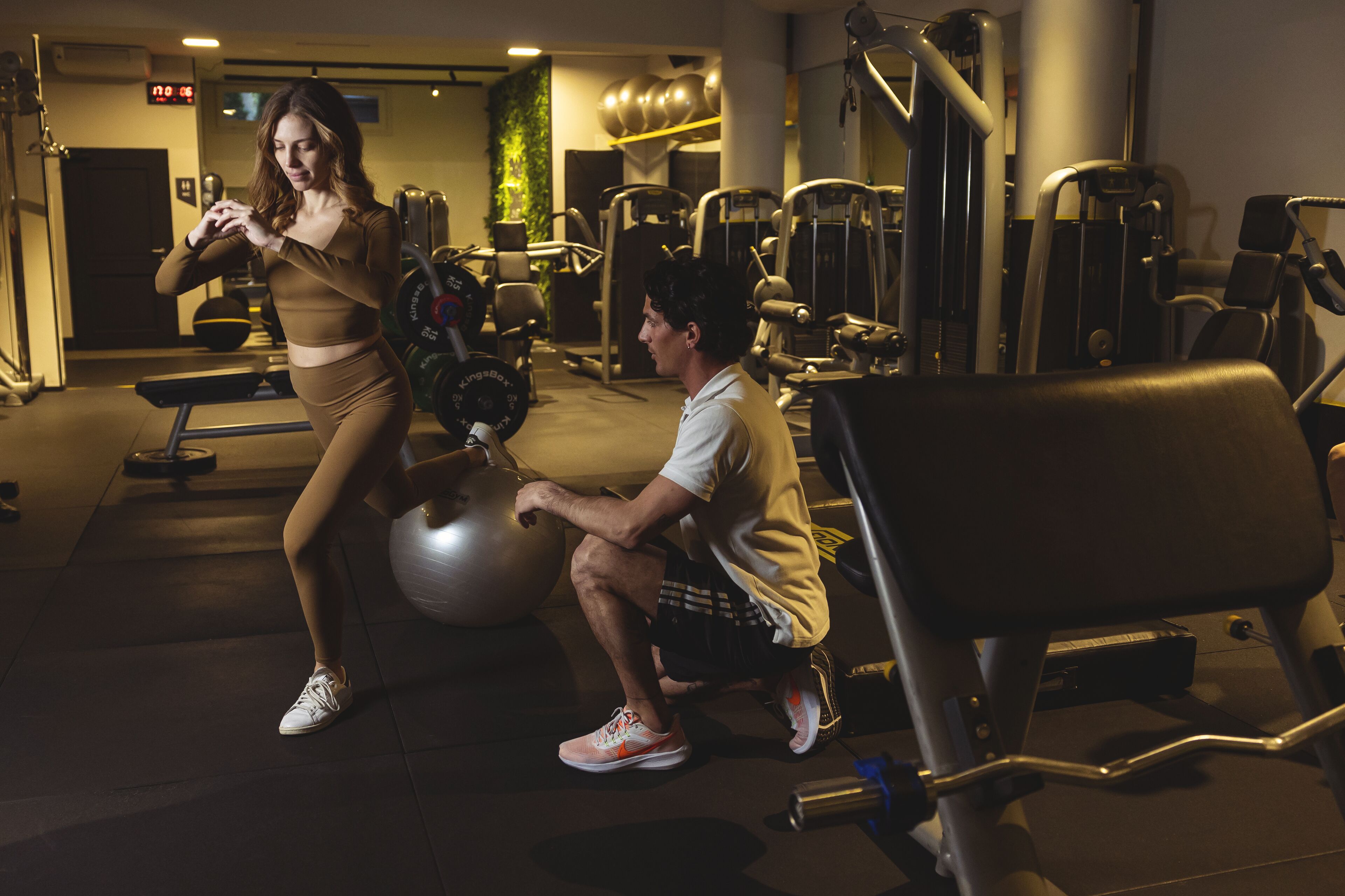 Un gimnasio con equipo de ejercicio, un reloj digital y una pared verde.