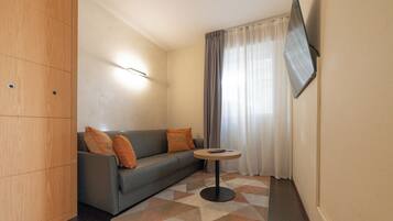 A modern living room with a grey sofa, orange cushions, a round coffee table, and a flat-screen TV mounted on the wall.