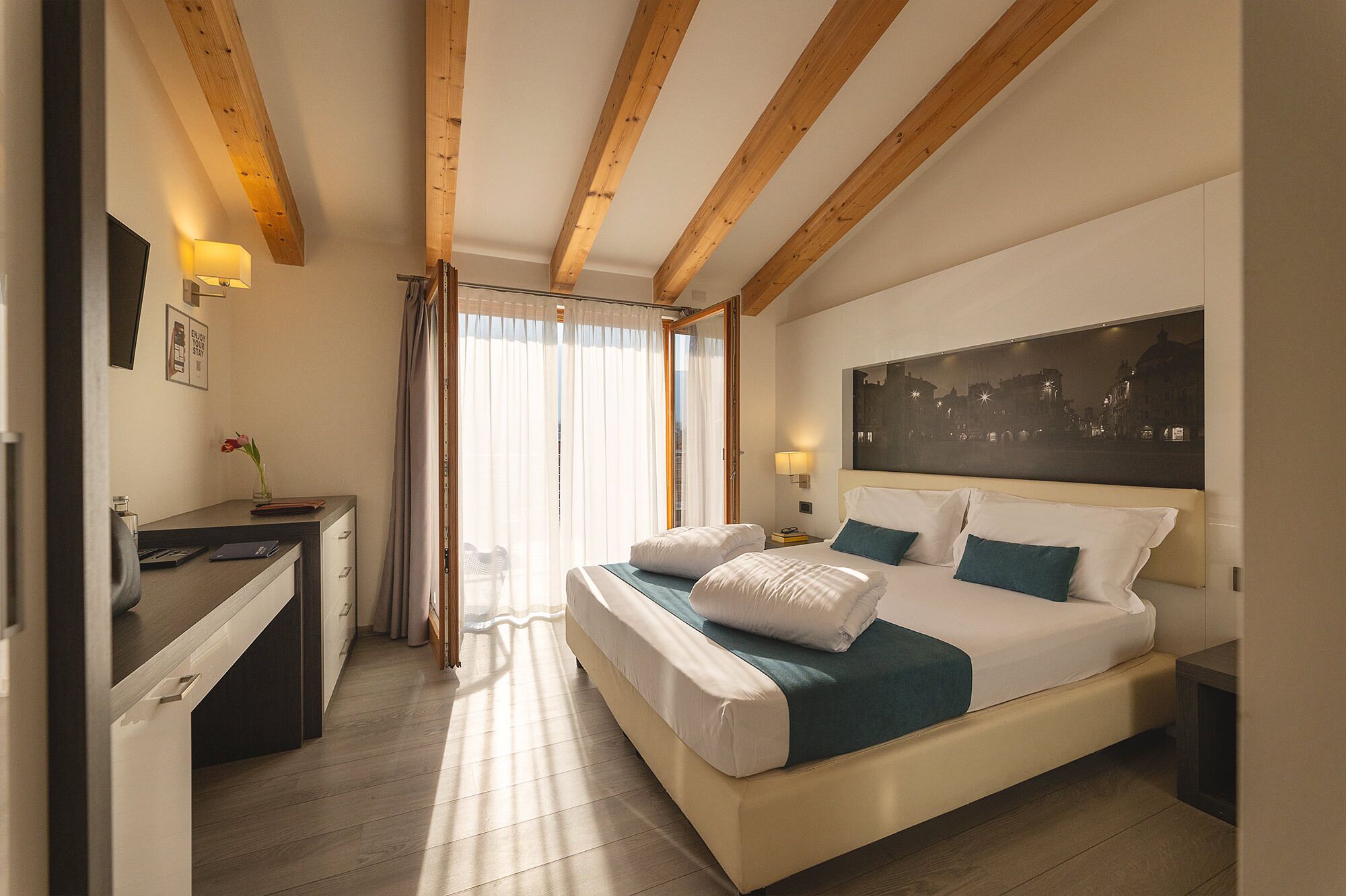 A hotel room with a bed, a desk, a chair, and a window with curtains.