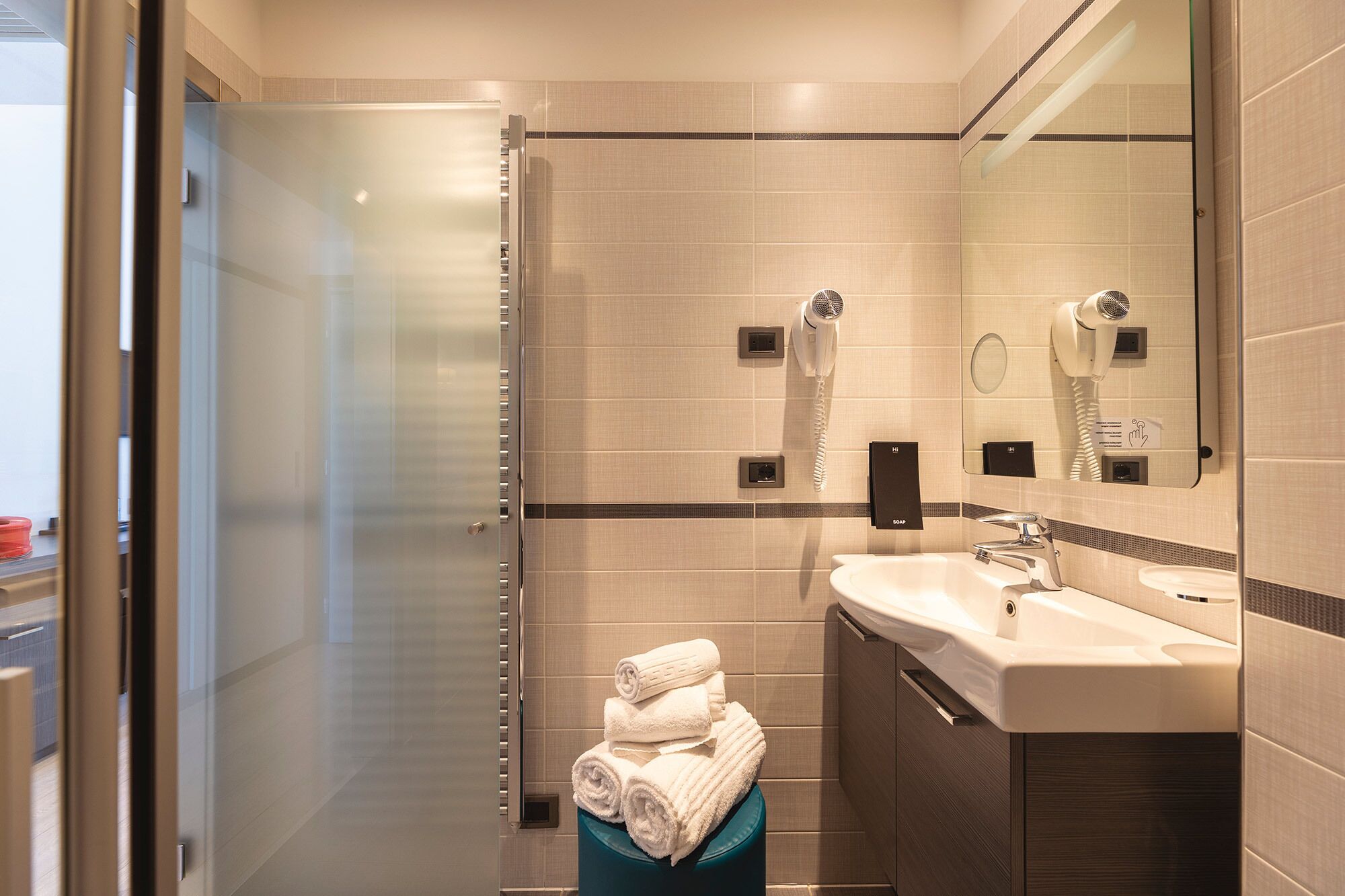 Une salle de bain moderne avec une douche à parois de verre, un lavabo avec un miroir et un porte-serviettes avec des serviettes pliées.
