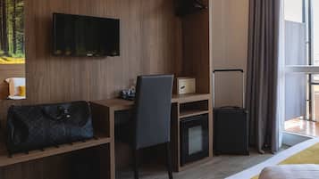 Habitació d'hotel amb escriptori de fusta, una cadira, un televisor fixat a la paret, un carro de roba i un llit.