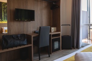 Ein Hotelzimmer mit einem Holztisch, einem Stuhl, einem an der Wand befestigten Fernseher, einem Gepäckwagen und einem Bett.