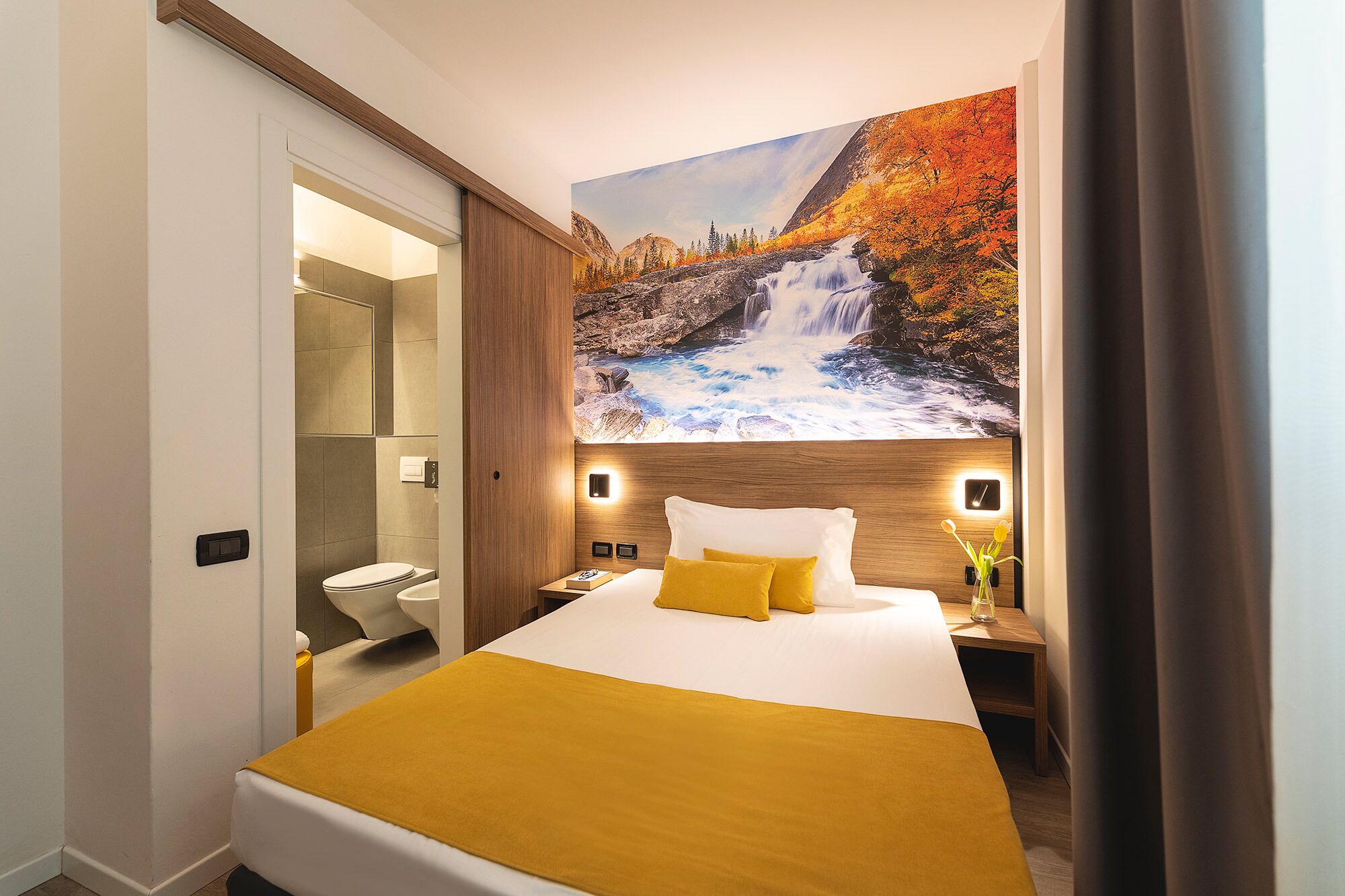 A hotel room with a bed, a bathroom, and a large mural of a waterfall.