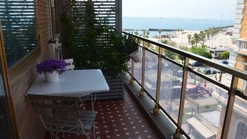A balcony with a table and chairs, potted plants, and a view of the sea and cityscape.