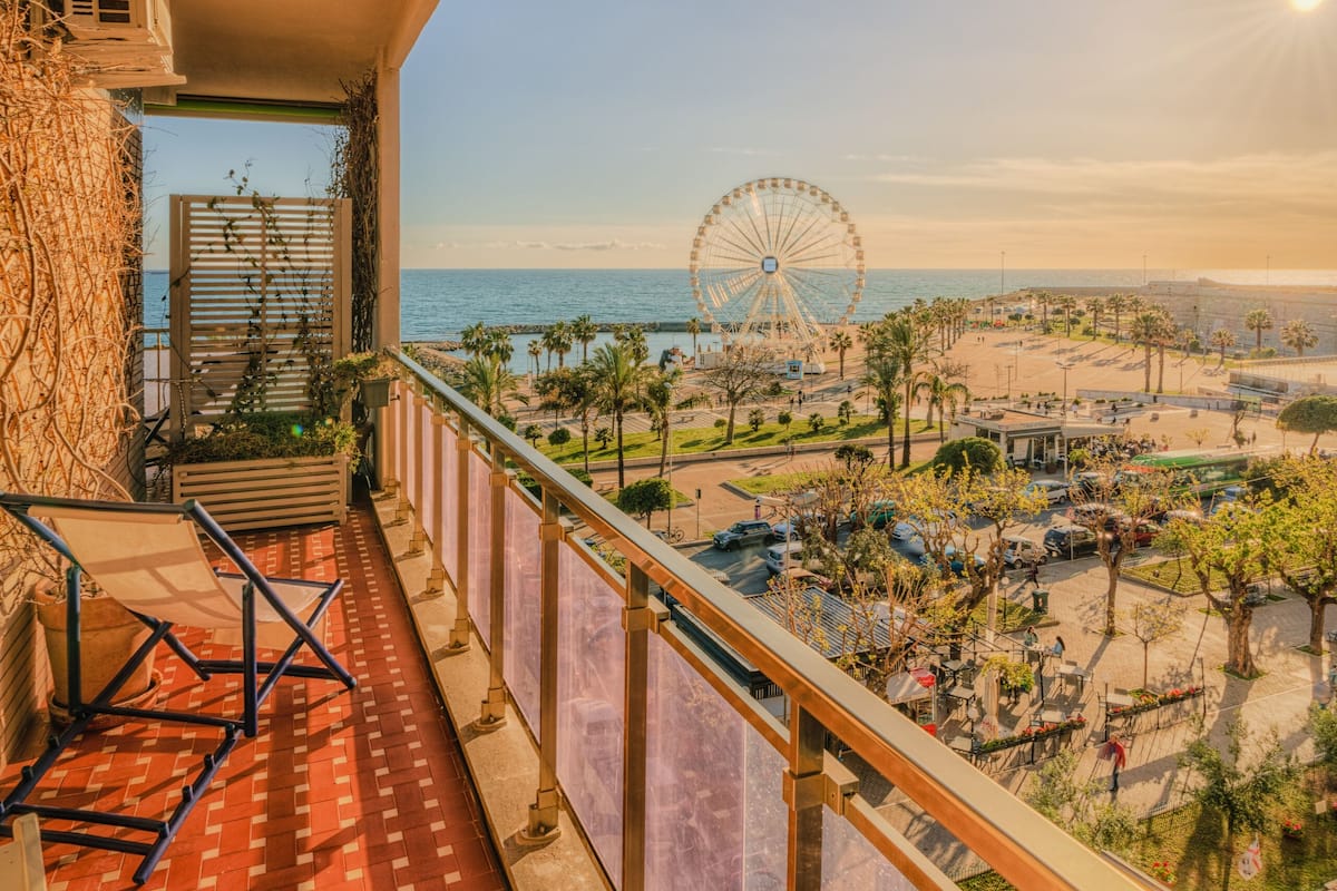 A balcony with a view of a beach, a Ferris wheel, and a clear sky.