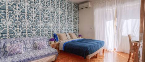 A bedroom with a patterned wall, a bed, a sofa, and a desk.