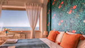 A hotel room with a bed, a view of the sea, a balcony with a table and chairs, and a window with curtains. - La Casa sul Mare (Civitavecchia)