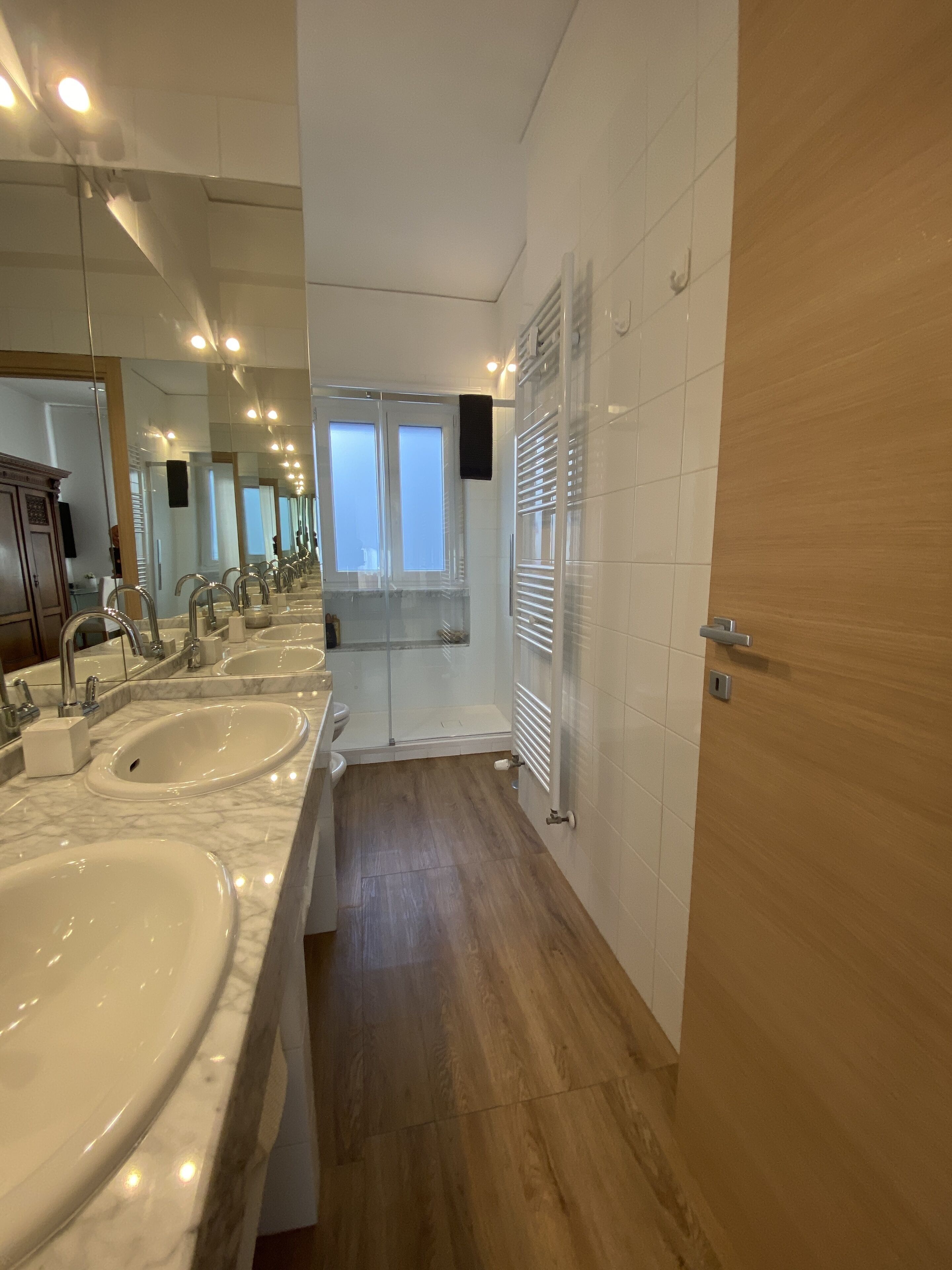 A modern bathroom with three sinks, a large mirror, and a wooden floor.
