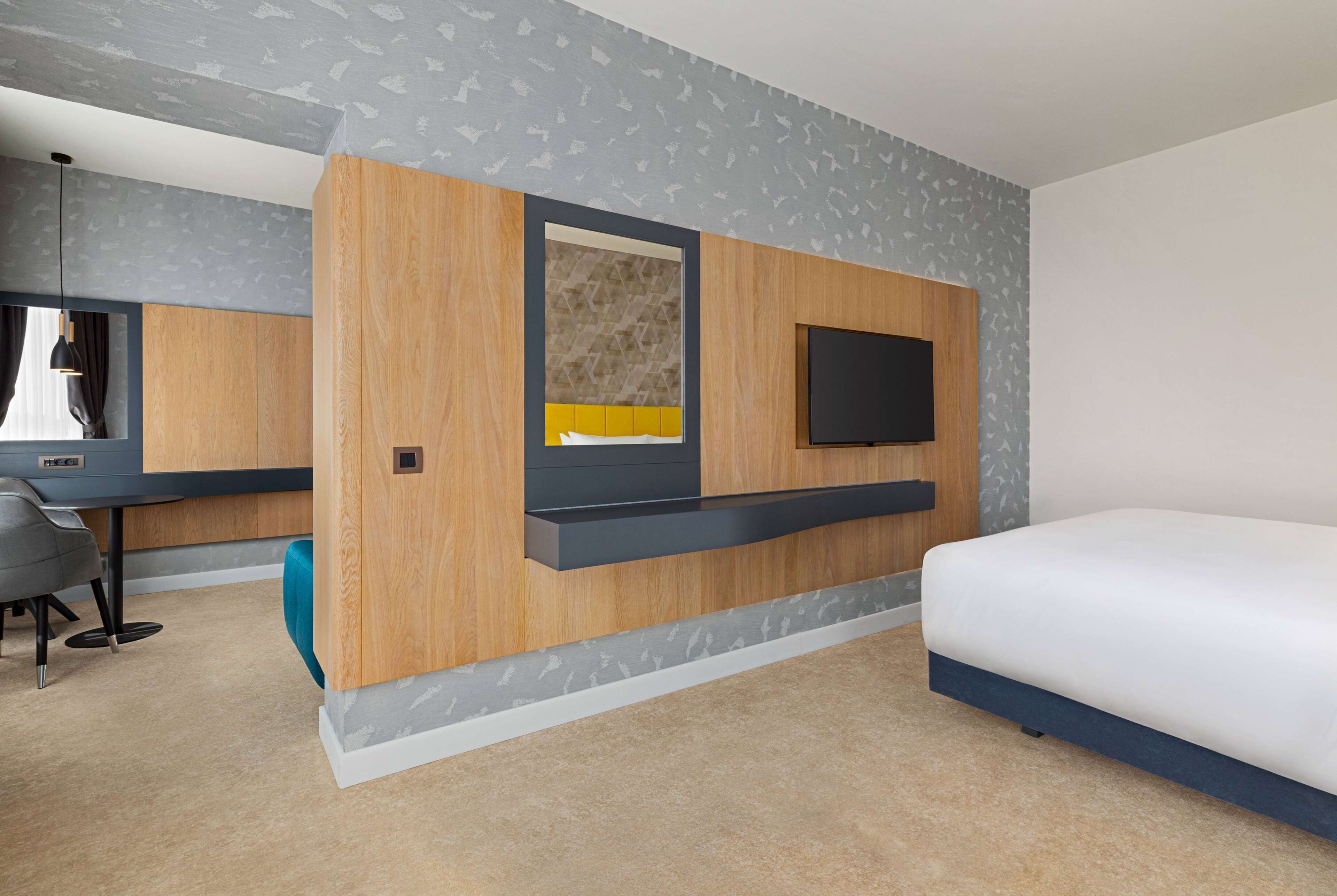 A modern hotel room with a wooden accent wall, a built-in desk, a flat-screen TV, and a large bed.