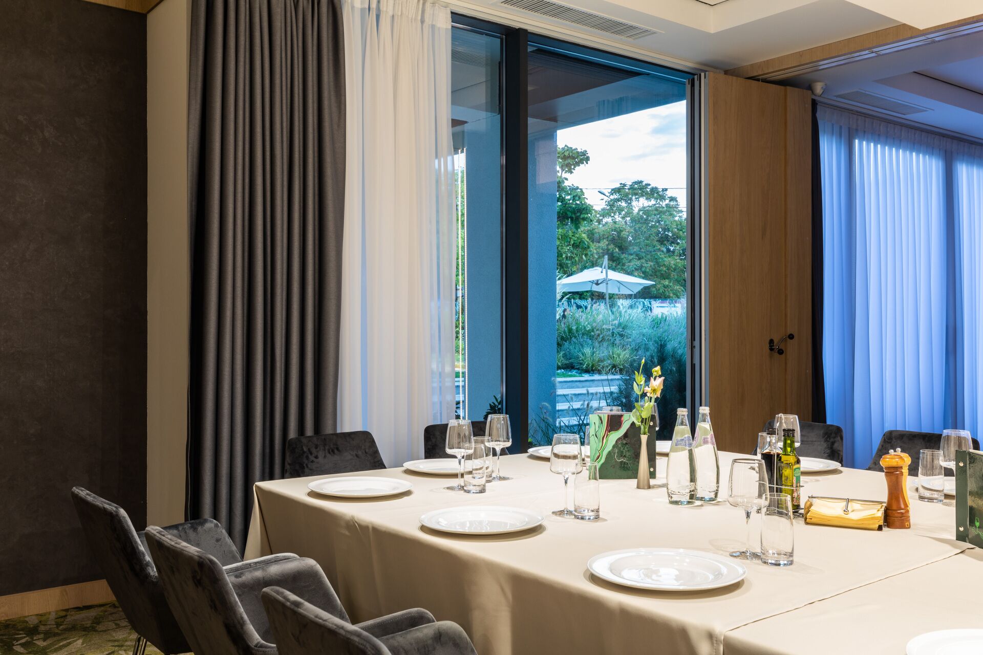 A dining area with a table set for six, large windows, and a view of greenery outside.