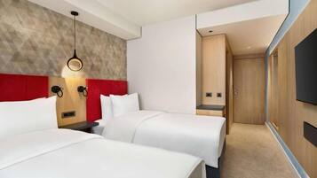 A hotel room with two beds, a red accent wall, a wooden headboard, a wall-mounted TV, and a modern light fixture.