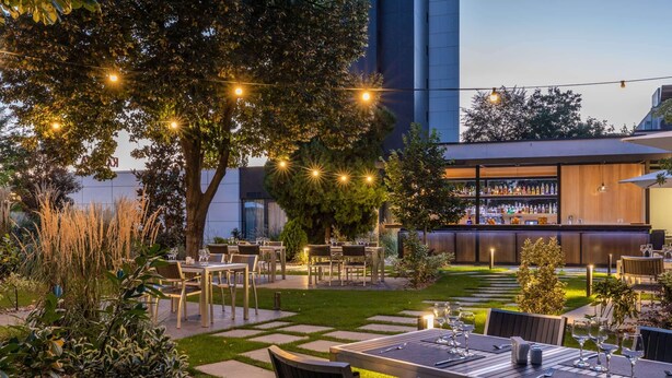 An outdoor dining area with tables and chairs, string lights, and a bar area with bottles.