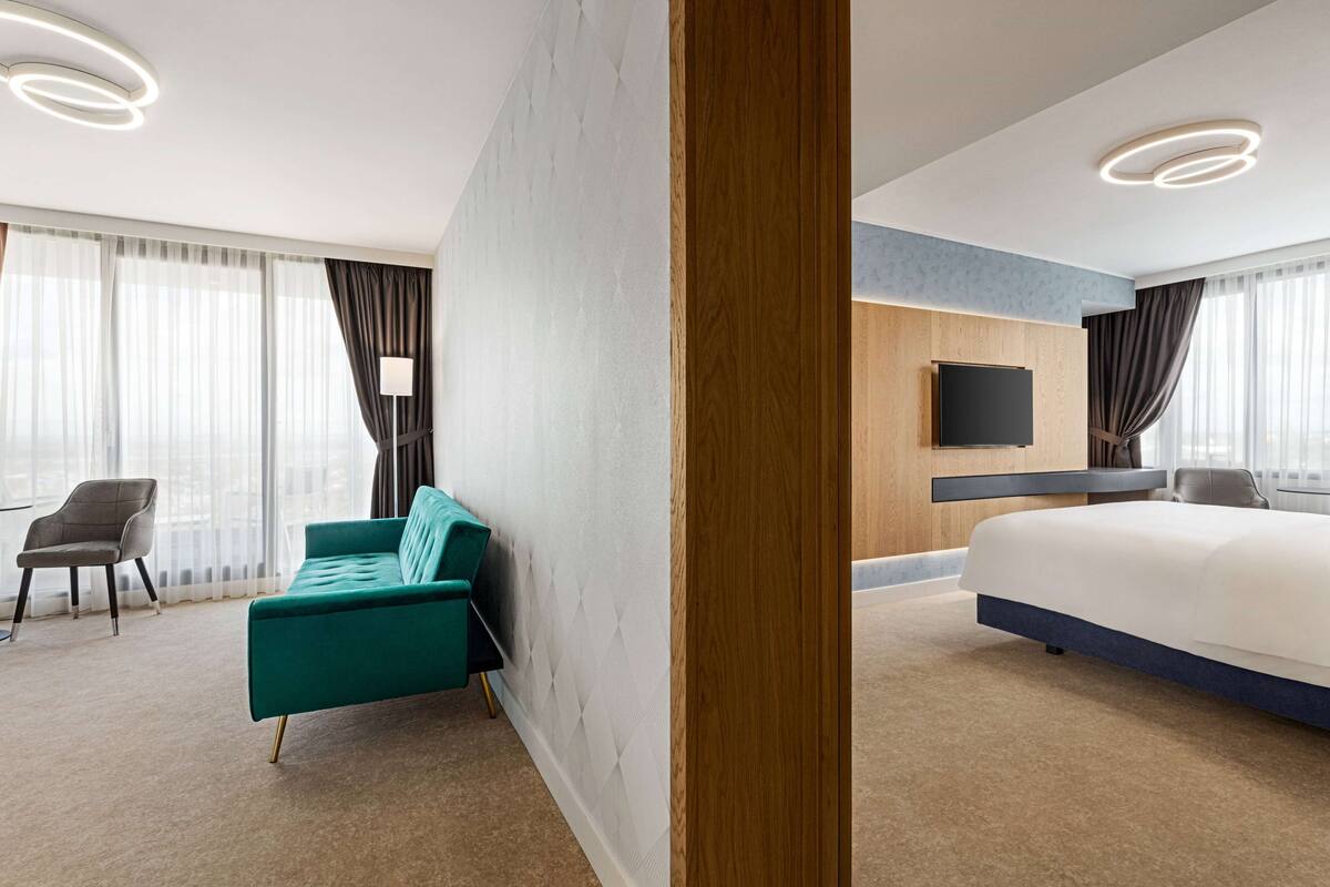 Una habitación de hotel moderna con una cama grande, un sofá verde, un televisor de pantalla plana y una pared de acento de madera.