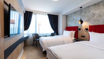 A hotel room with two beds, a desk, a chair, and a large window with curtains.