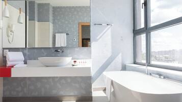 A modern bathroom with a large window, a freestanding bathtub, and a vanity with a large mirror.