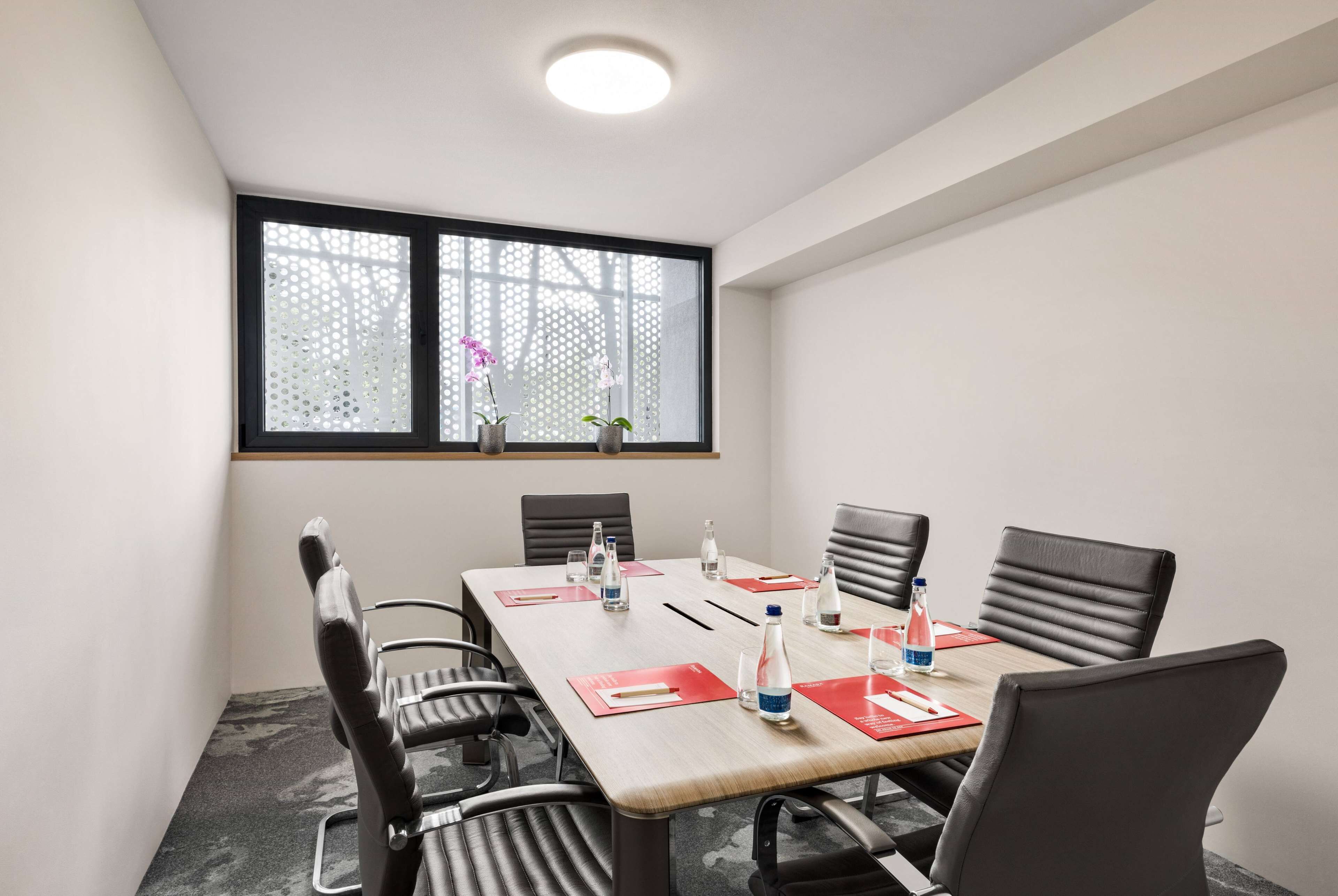 A conference room with a large table, black chairs, and a window with a view of the outside.