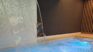 A hot tub with a blue light effect, surrounded by a tiled wall and a wooden panel.