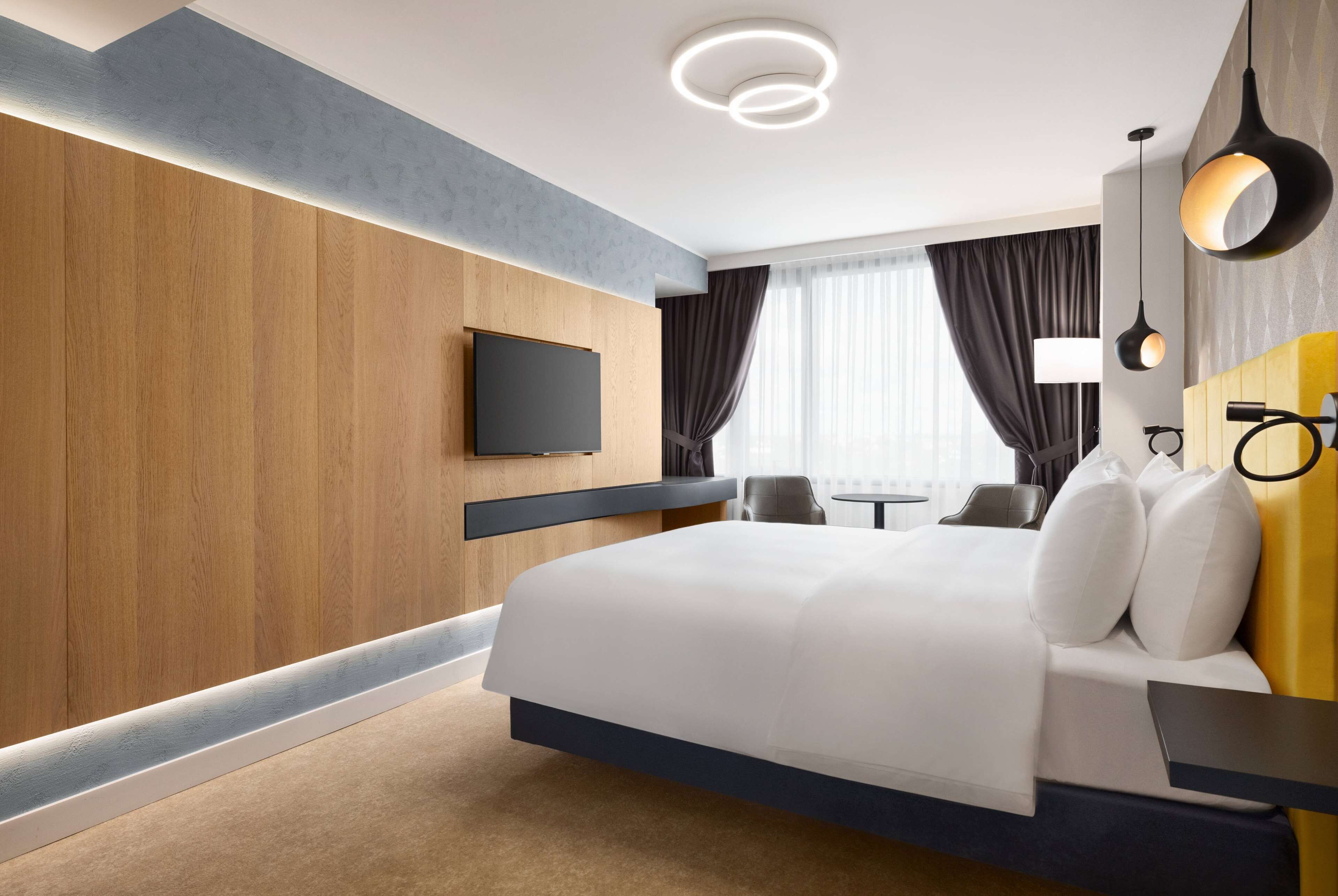 A modern hotel room with a large bed, a flat-screen TV, a small table, and a sofa.