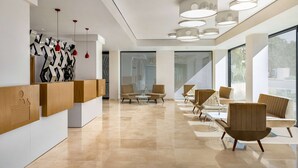 A modern reception area with a wooden reception desk, seating area with chairs and tables, and a large window providing a view of the outdoors.