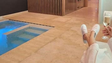 Una persona relajándose en el suelo, con una copa de vino, cerca de una piscina pequeña con un borde iluminado en azul.