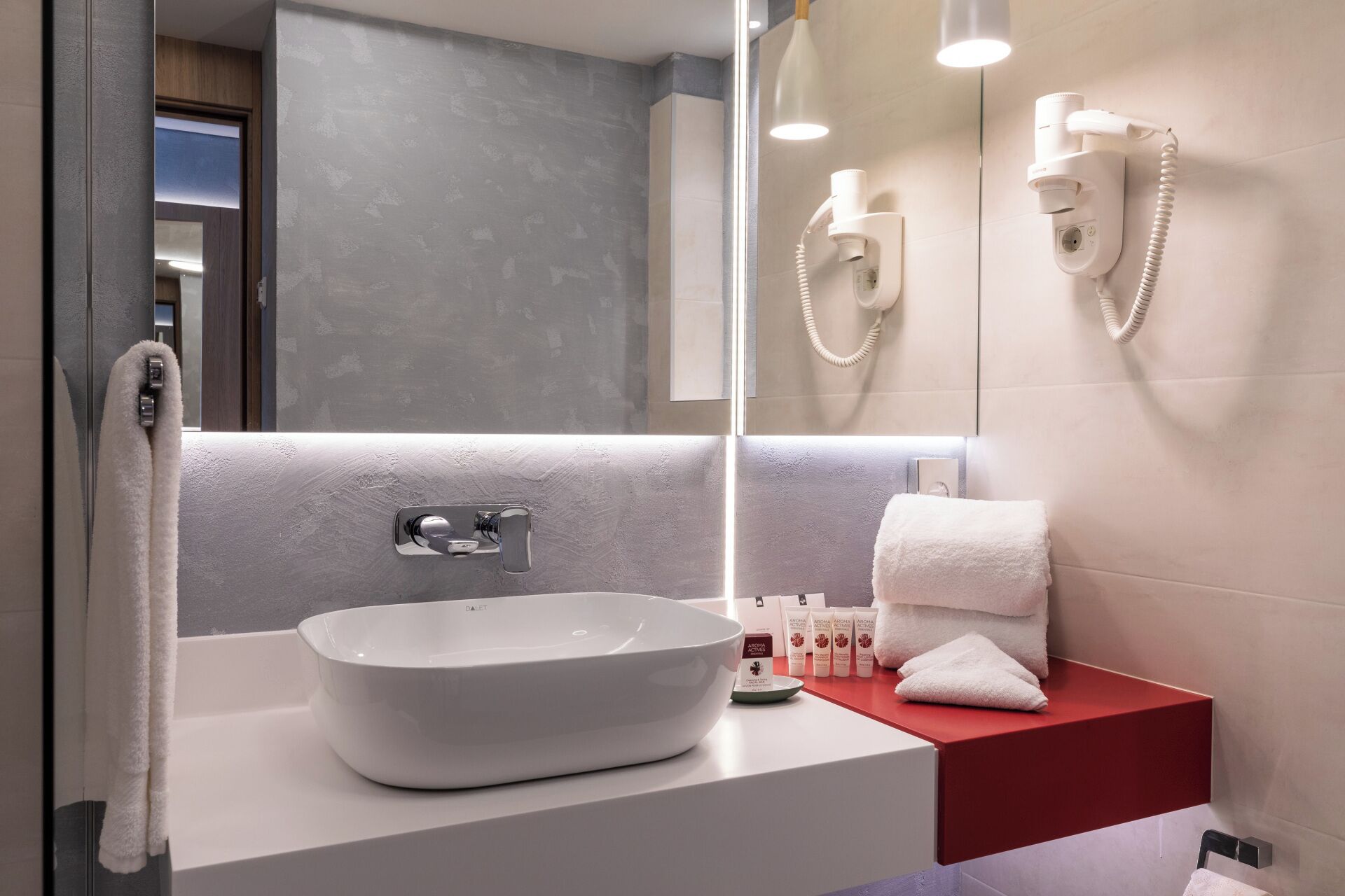 Un bagno moderno con un grande specchio, un lavandino bianco e un piano d'appoggio rosso.
