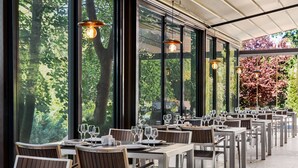 An outdoor dining area with tables and chairs, large windows, and hanging pendant lights.