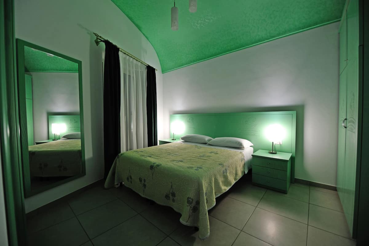 Ein Schlafzimmer mit einem Bett, Nachttischen, einem Spiegel und einer grünen Decke.